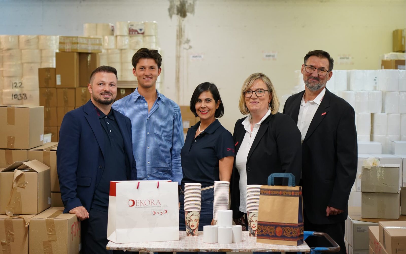 Team von Dekora Packaging mit Tragetaschen, Bechern und Verpackungen im Lager